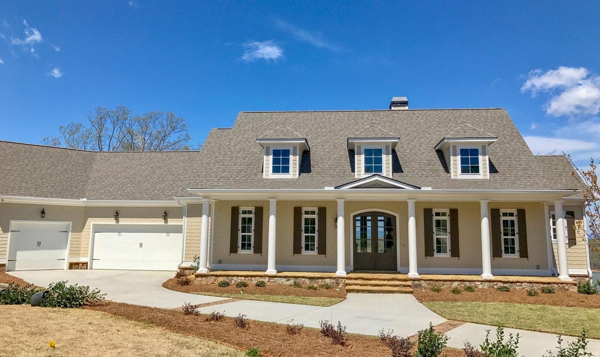 House plan exterior featuring a prominent covered porch with columns, multiple gables, dormer windows, and a side-entry three-car garage.