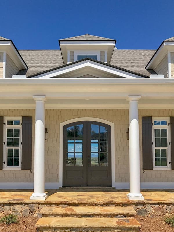 House plan exterior: Covered front porch with Doric columns, double arched glass doors, dormers, and gable rooflines.