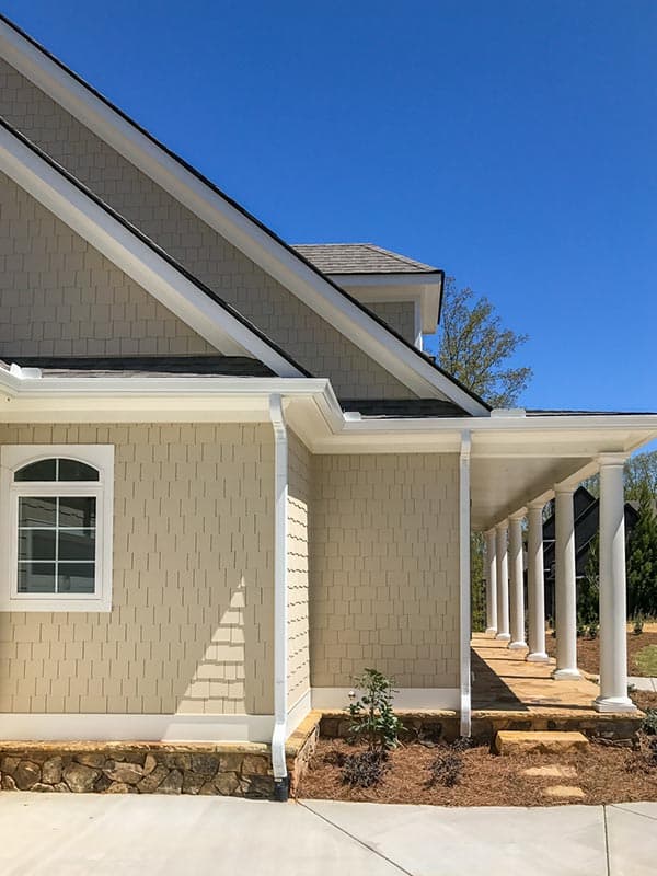 House plan exterior with shingle siding, arched window, stone foundation, and a covered porch with columns.