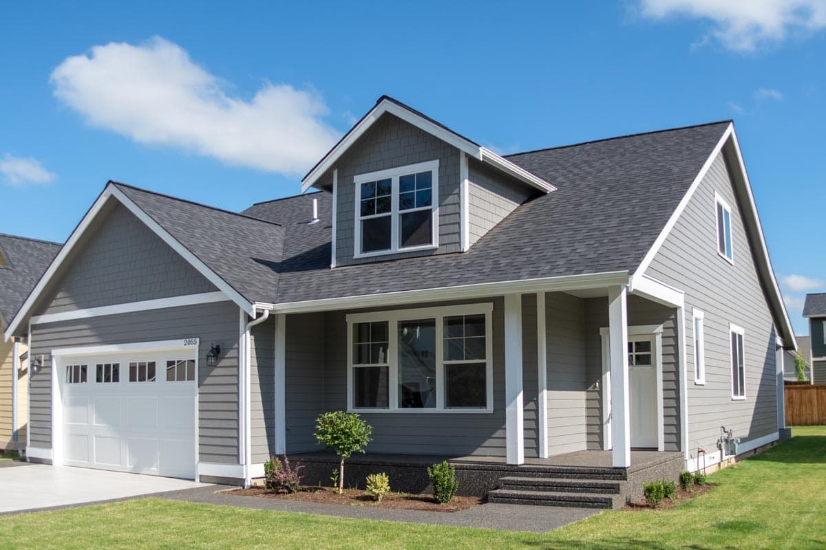 House plan exterior. Two-story, Craftsman-style home with a front porch, gables, and a dormer. Features a two-car garage and dark gray roof.