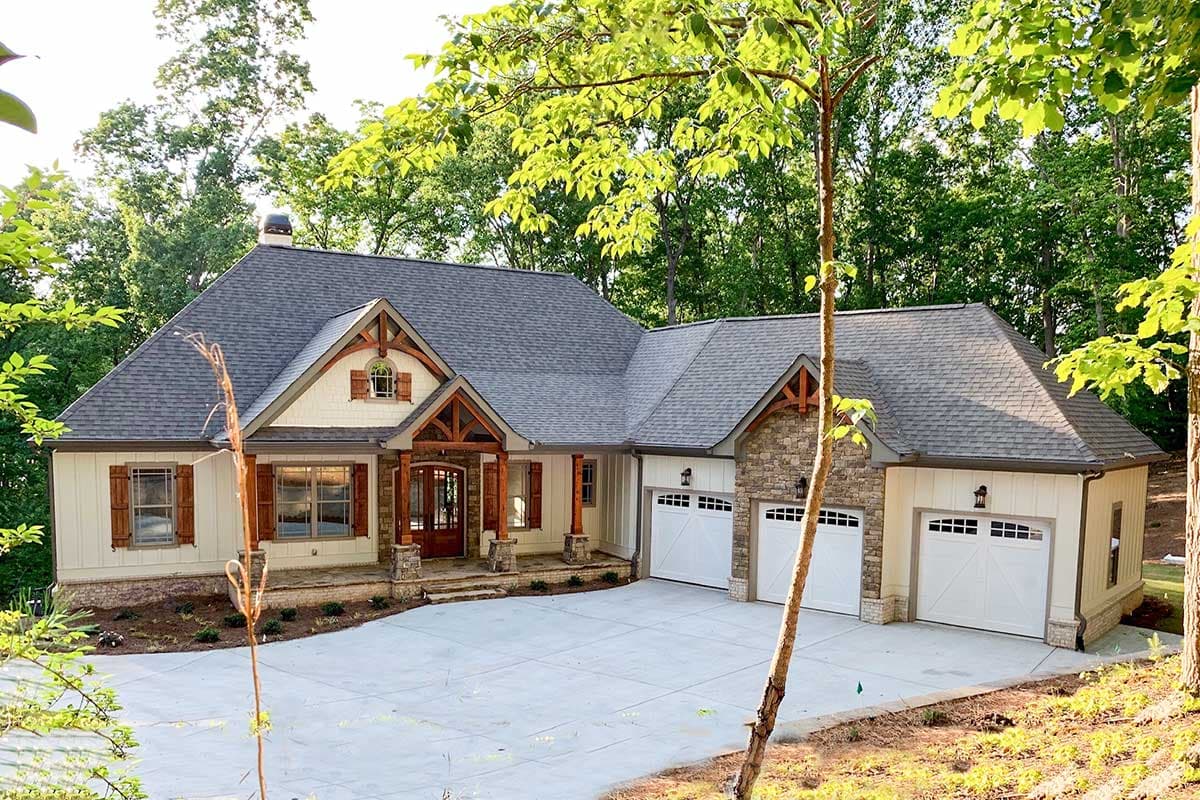 House plan exterior: Ranch style, one-story, covered entry porch with timber accents, stone and board-and-batten siding, three-car garage.