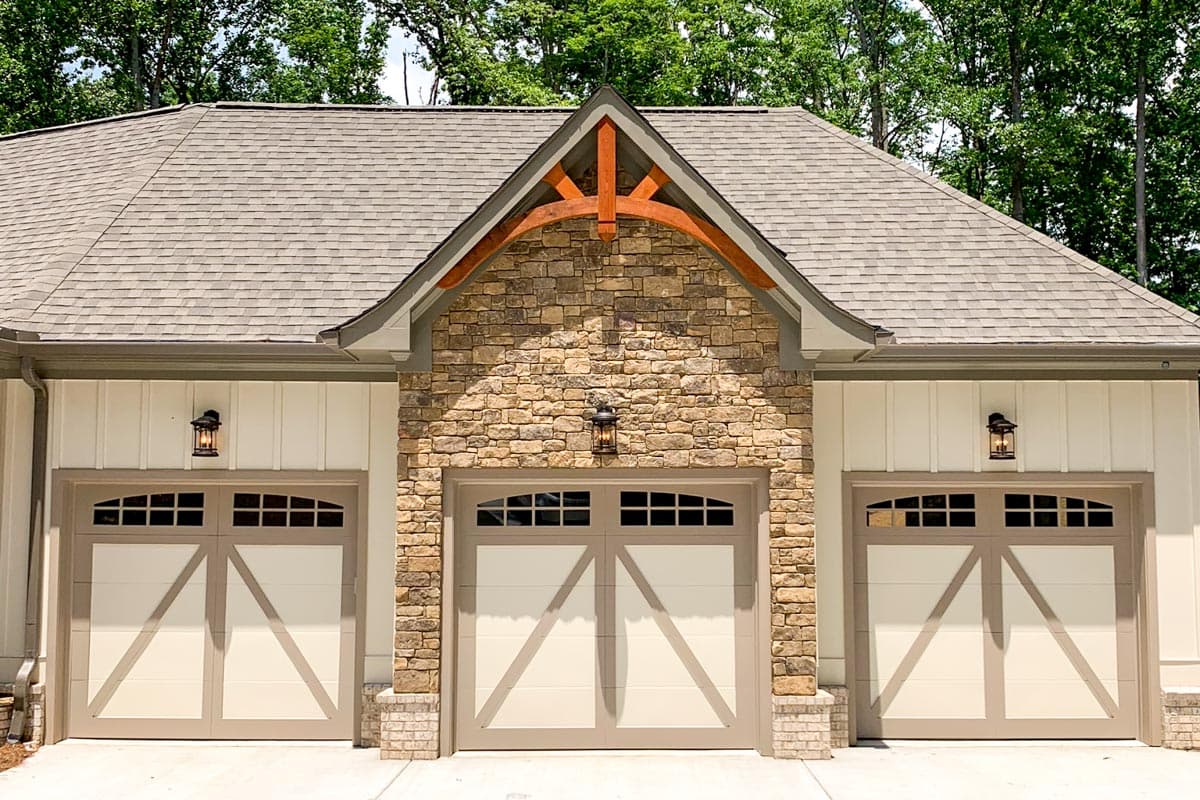 House plan exterior featuring three garage bays with arched windows, stone accents, and decorative wood truss.