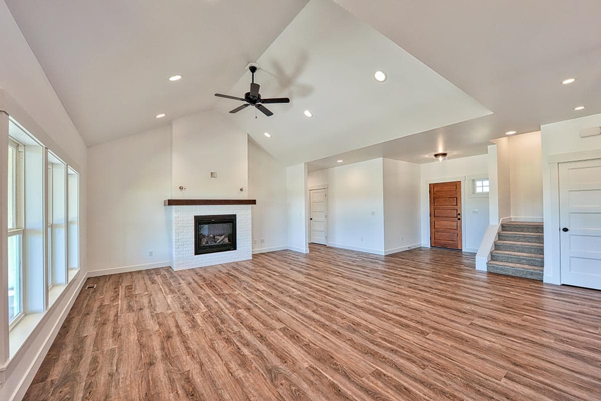 Interior rendering of a great room with a vaulted ceiling, brick fireplace, wood-look flooring, and a wooden front door.