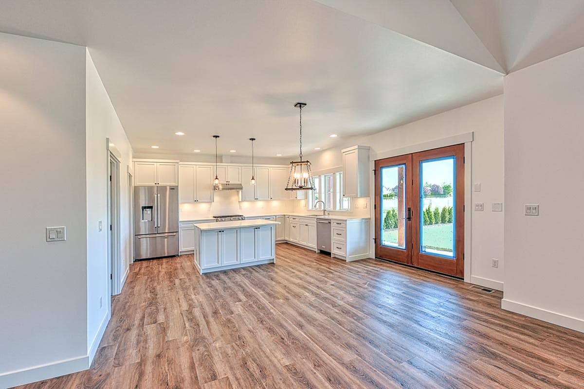 Open-plan kitchen with white cabinets, large island, stainless steel appliances, and double doors to outdoor space.
