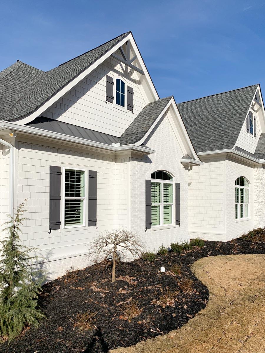 House plan exterior featuring shingle and brick siding, multiple gables with decorative trusses, and arched windows with shutters.