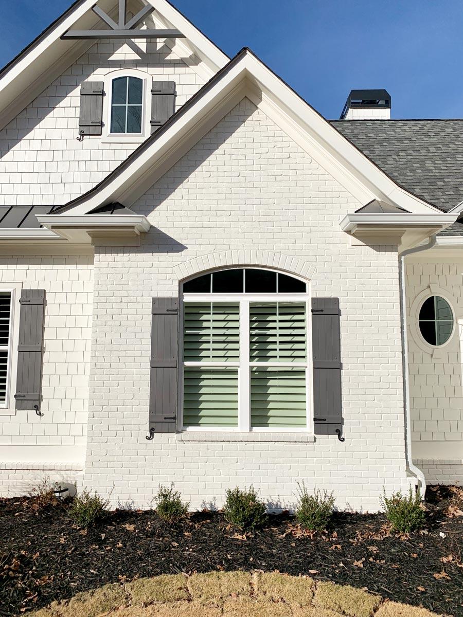 House plan exterior with white brick, shake siding, dormer windows, gabled rooflines, and decorative shutters.