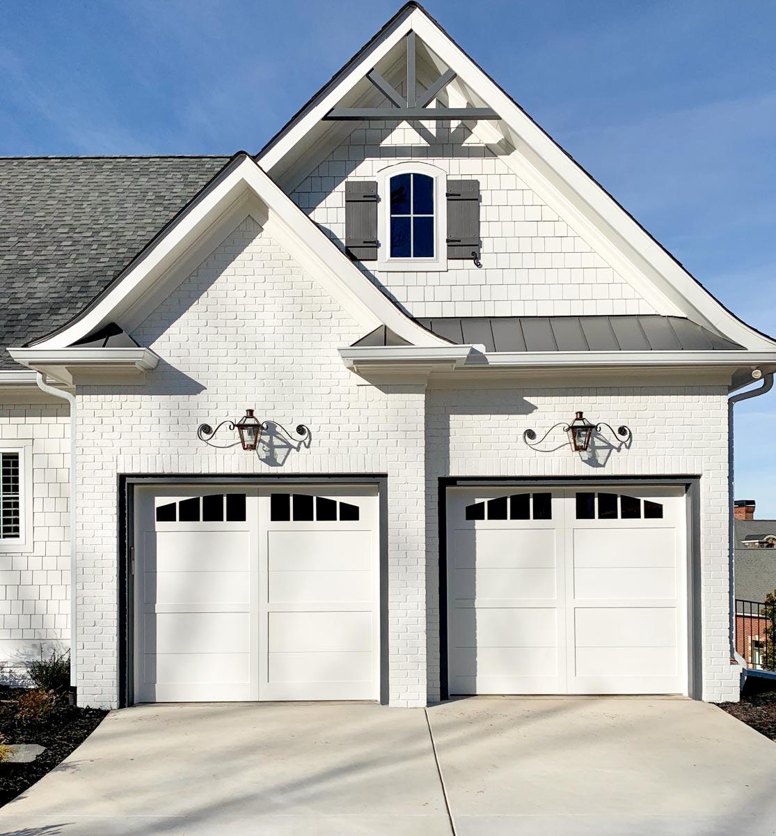 House plan exterior featuring white brick and siding, a gable with decorative brackets, and two garage doors with arched windows.