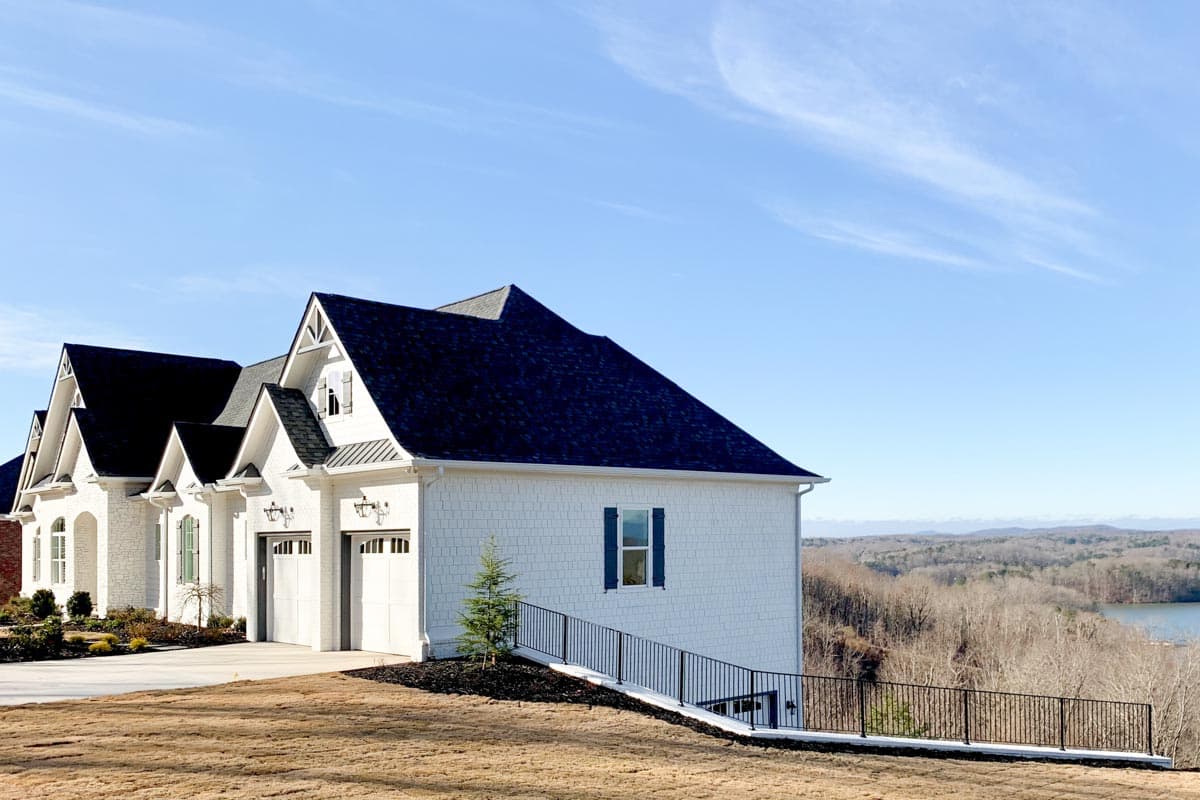 House plan exterior with white shake siding, multiple gables, a dark roof, and a three-car garage.