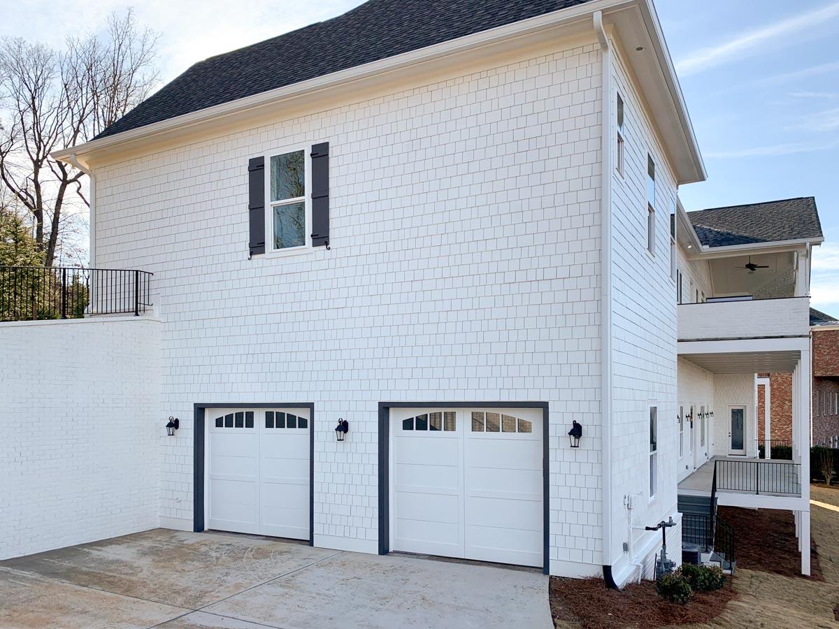 House plan exterior featuring white cedar shakes, two garage doors with arched windows, and a covered balcony.