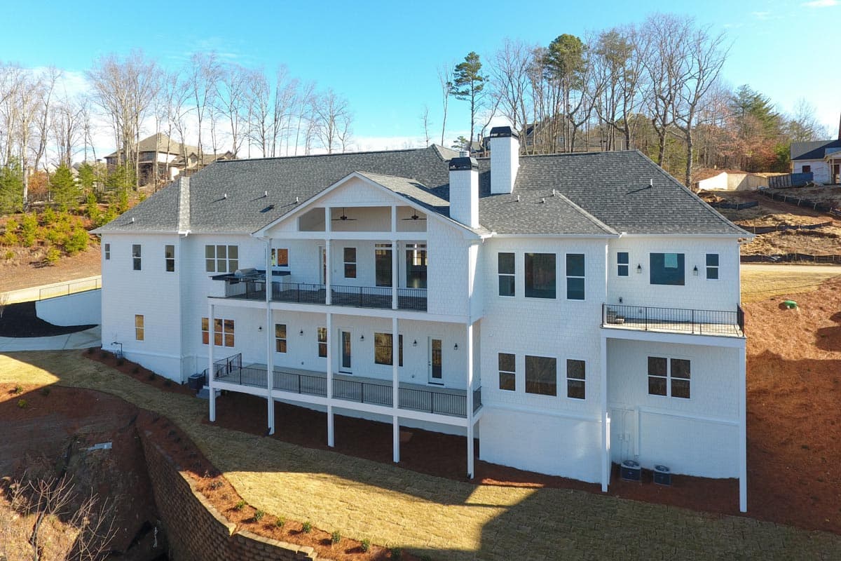 Modern house plan exterior with multiple levels, covered balconies, white shingle siding, and dual chimneys.
