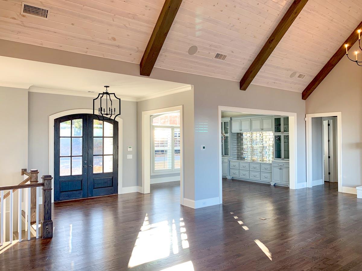 Interior view: Open layout with vaulted ceiling, exposed wood beams, double entry doors, and built-in cabinetry.