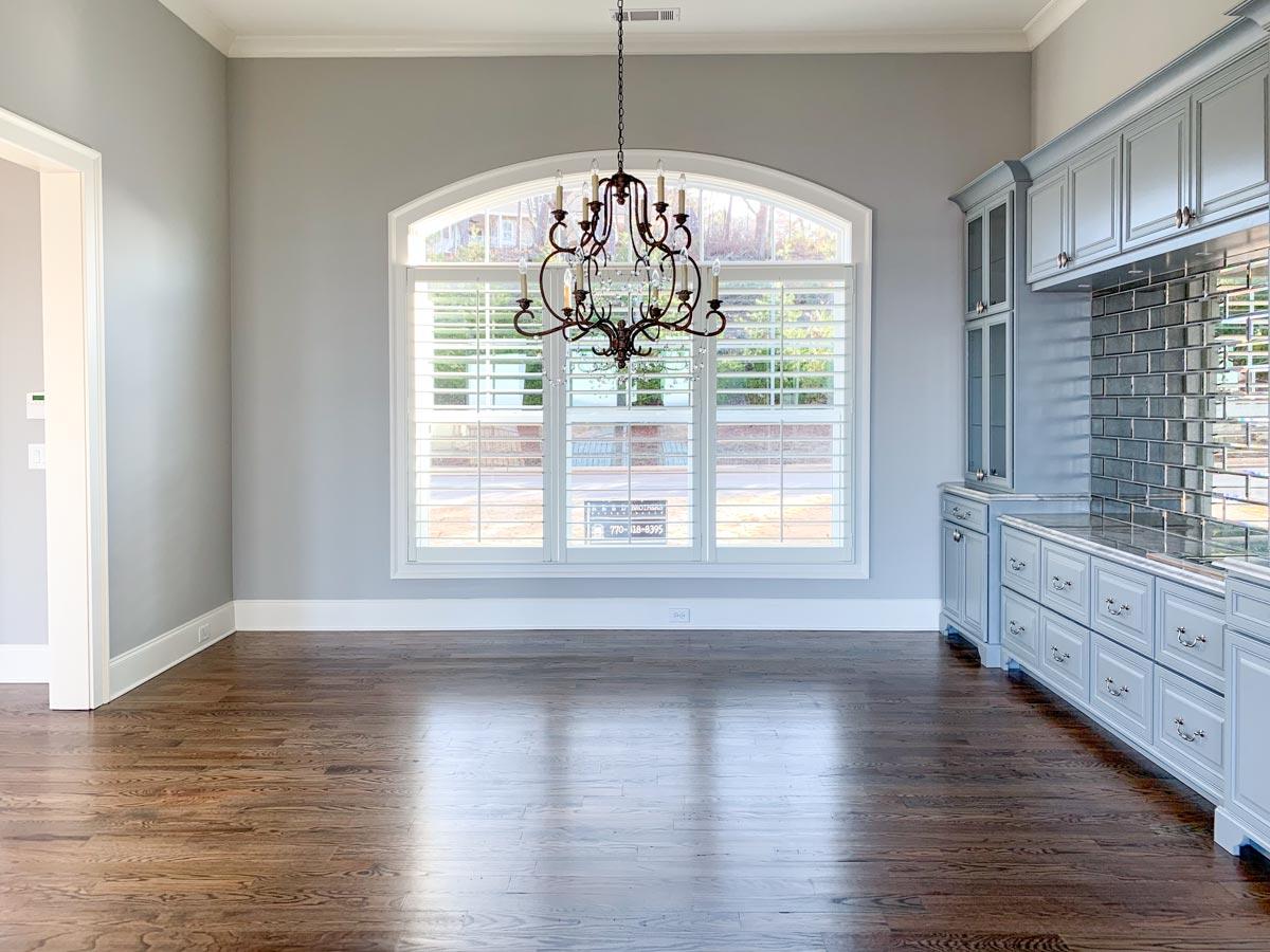 Interior view of a dining area or kitchen with light blue cabinetry, mirrored backsplash, hardwood floors, and arched window with shutters.