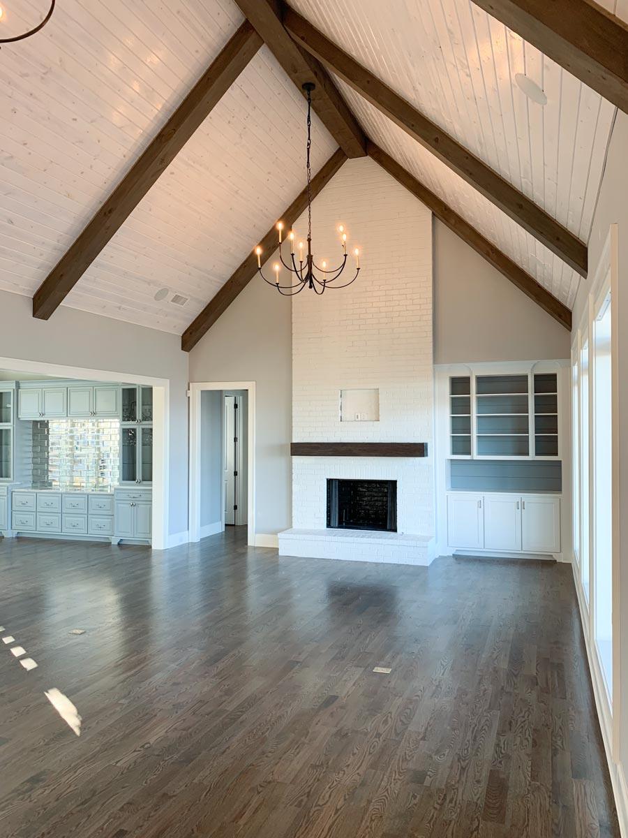 Living room with vaulted wood-beamed ceiling, white brick fireplace, built-in cabinetry, and hardwood floors.