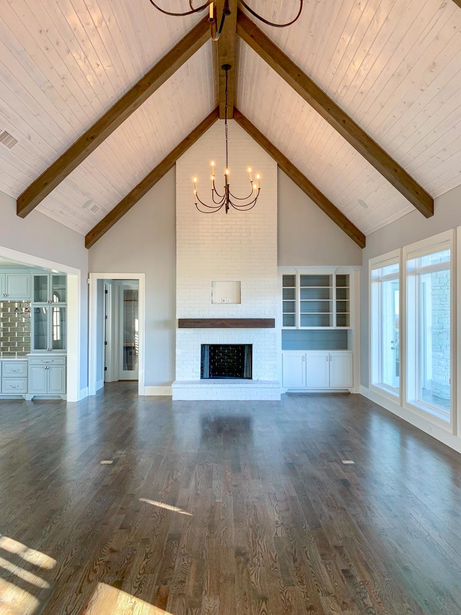 Interior view of a great room with vaulted wood-beamed ceiling, brick fireplace, and built-in cabinets.
