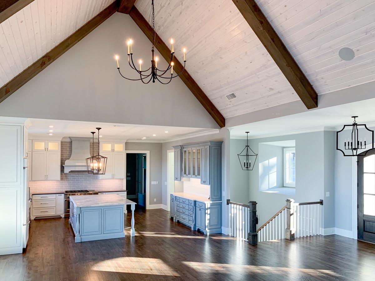 Open concept great room and kitchen with vaulted wood plank ceiling, exposed beams, island, and staircase.