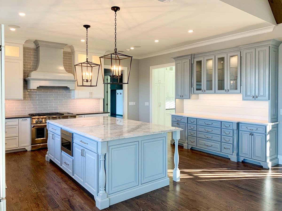 Kitchen interior with light blue island, grey subway tile backsplash, stainless steel range, and built-in cabinetry.