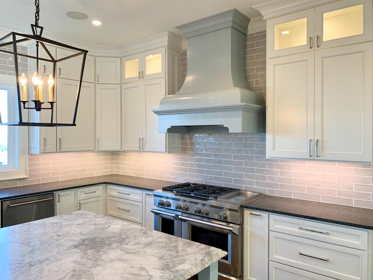 Kitchen with white cabinets, gray subway tile backsplash, large range, and marble island.
