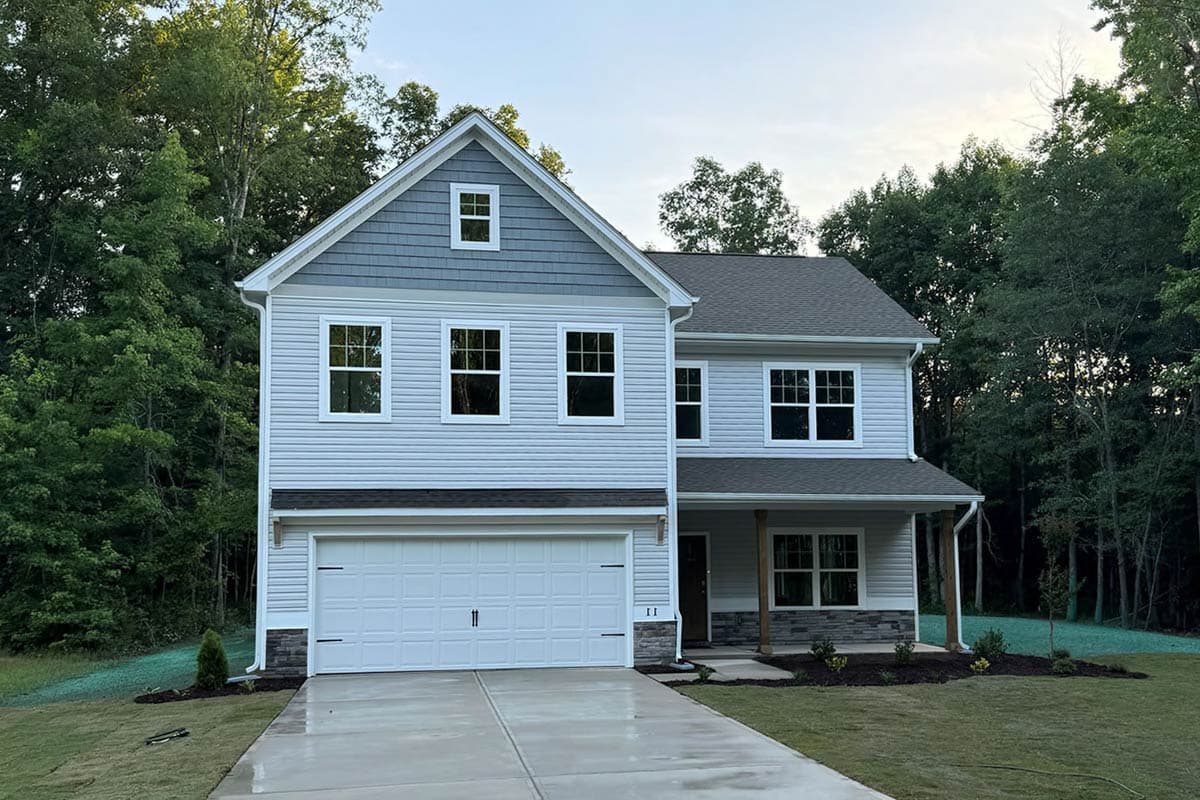 Two-story house plan exterior with a gable dormer, double garage, and a covered front porch with stone accents.