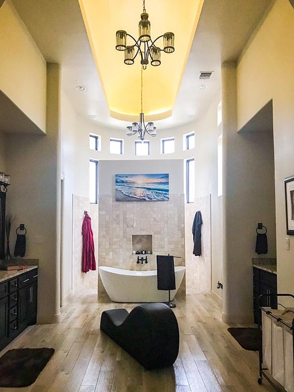Spacious bathroom with freestanding tub, dual vanities, and high, vaulted ceiling with chandeliers.