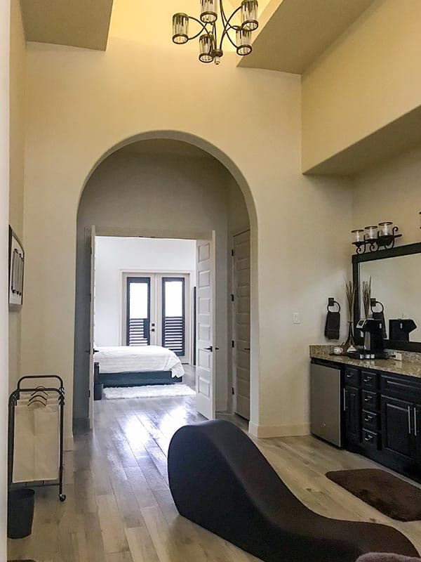 Interior view of a bedroom and wet bar area, featuring an arched entryway, vaulted ceiling, and wood plank flooring.