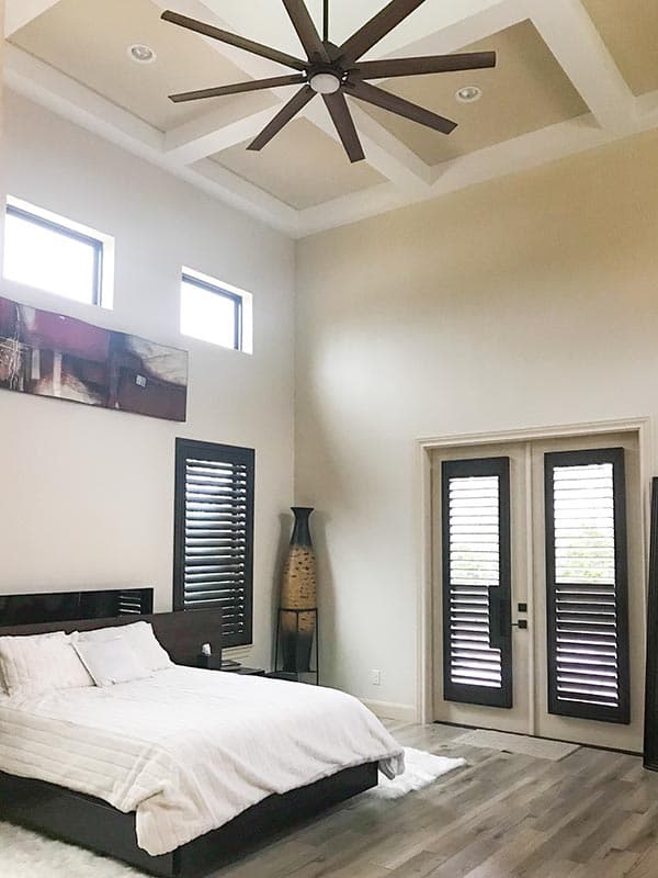 Bedroom with coffered ceiling, large ceiling fan, tall windows, and double doors with shutters.