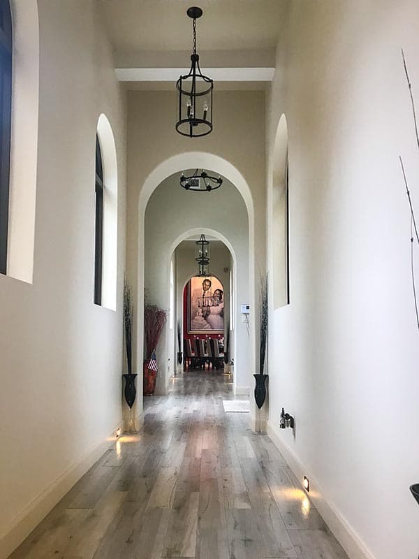 Hallway with arched doorways, pendant lights, and wood plank flooring leading to a framed artwork.