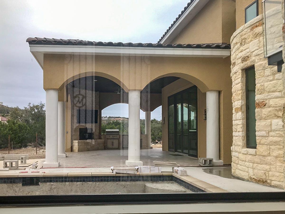 House plan exterior: stucco walls, arched loggia with columns, outdoor kitchen, and stone exterior.