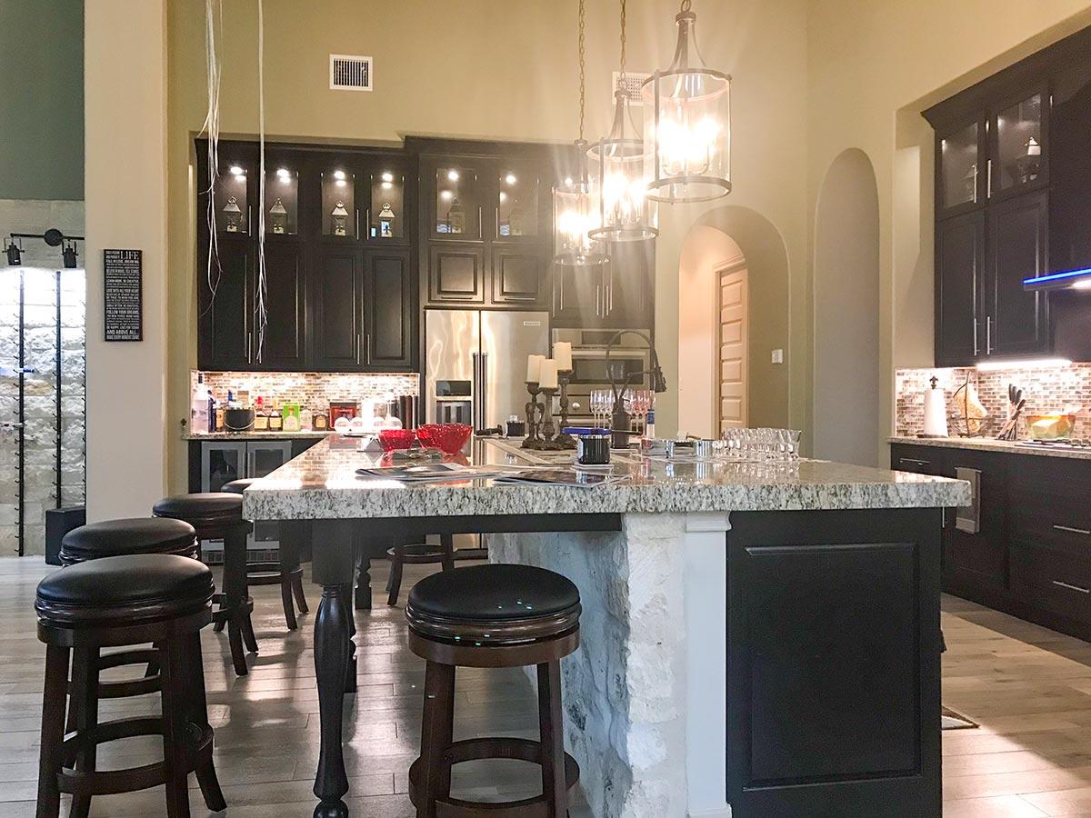 Kitchen interior with dark cabinets, granite-topped island with bar stools, stainless steel appliances, and pendant lighting.