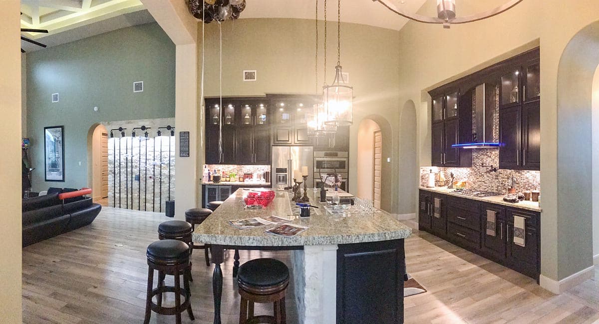 Open concept kitchen with large island, dark cabinetry, tile backsplash, and vaulted ceiling with exposed beams.