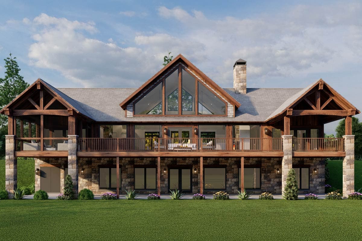House plan exterior: Mountain style, two stories, prominent A-frame gable with large windows, stone chimney, extensive wooden decks and exposed beams.