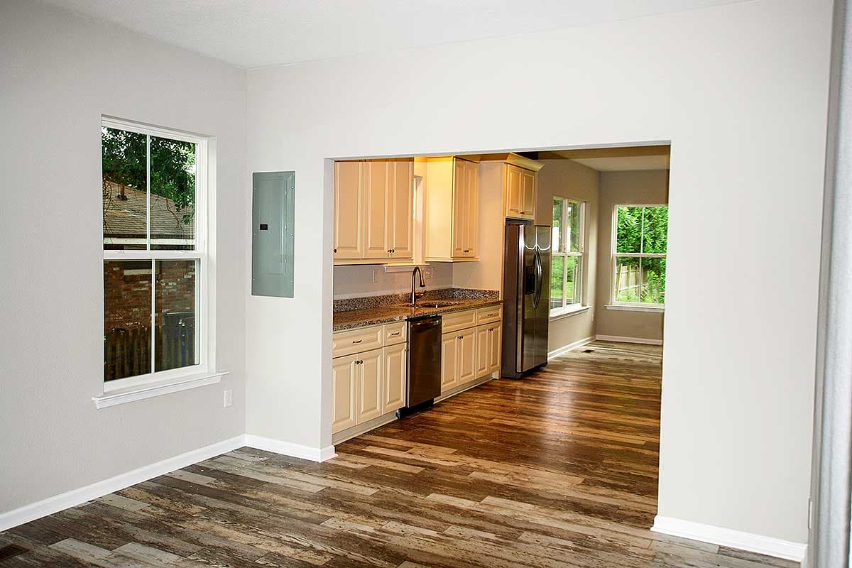 Interior view of a kitchen with cream cabinets, granite countertops, stainless steel refrigerator and dishwasher, opening to dining area.