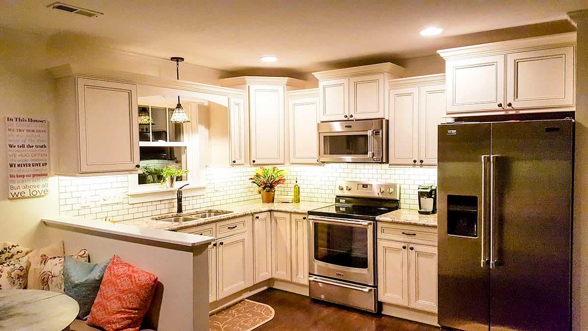 Kitchen interior with white cabinets, stainless steel appliances, subway tile backsplash, granite countertops, and a built-in banquette.