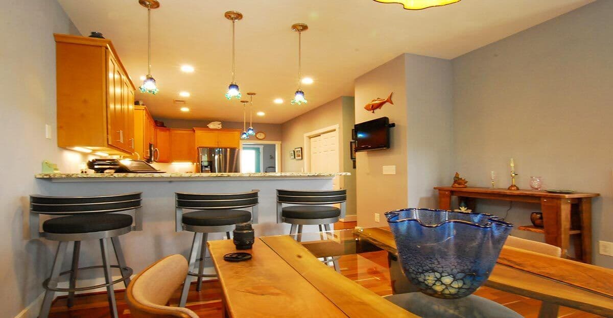 Kitchen and dining area with wood cabinets, granite countertop, bar seating, pendant lights, and a wooden console table.
