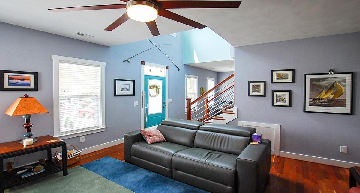 Interior view of living room with gray sofa, teal door, and open staircase leading to upper level.