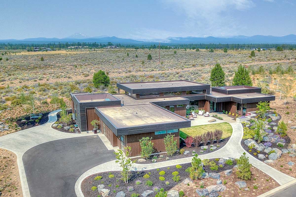 Modern house plan exterior with multiple flat-roofed volumes, wood siding, and extensive landscaping.