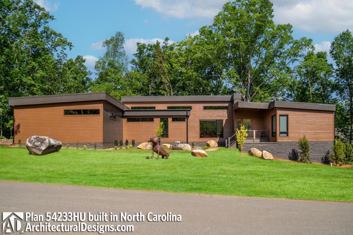 Modern house plan exterior with wood siding, a low-slope roof, horizontal windows, and a recessed entry with a porch.