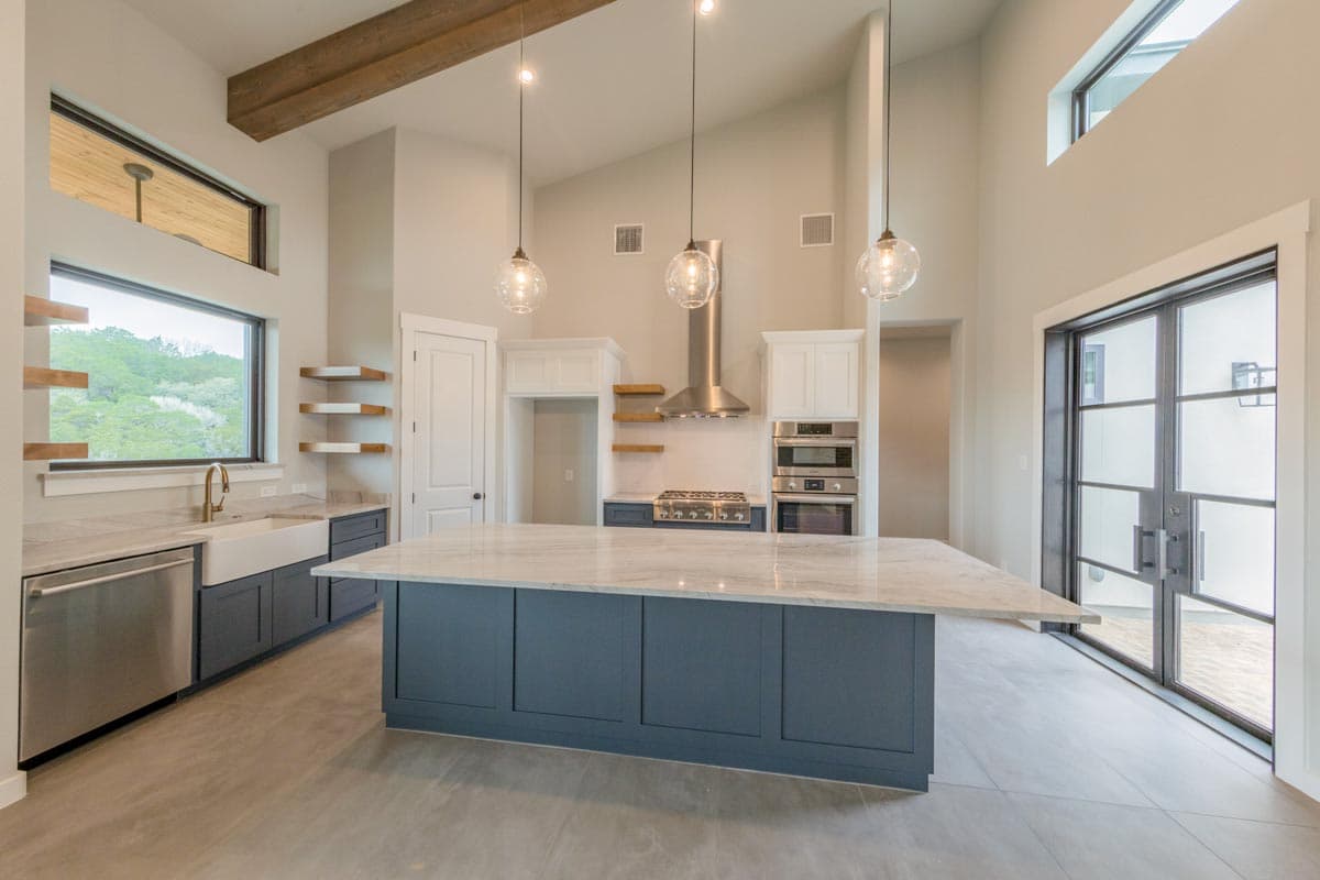 Modern kitchen with vaulted ceiling, exposed beams, large island with marble countertop, stainless steel appliances, and large windows.