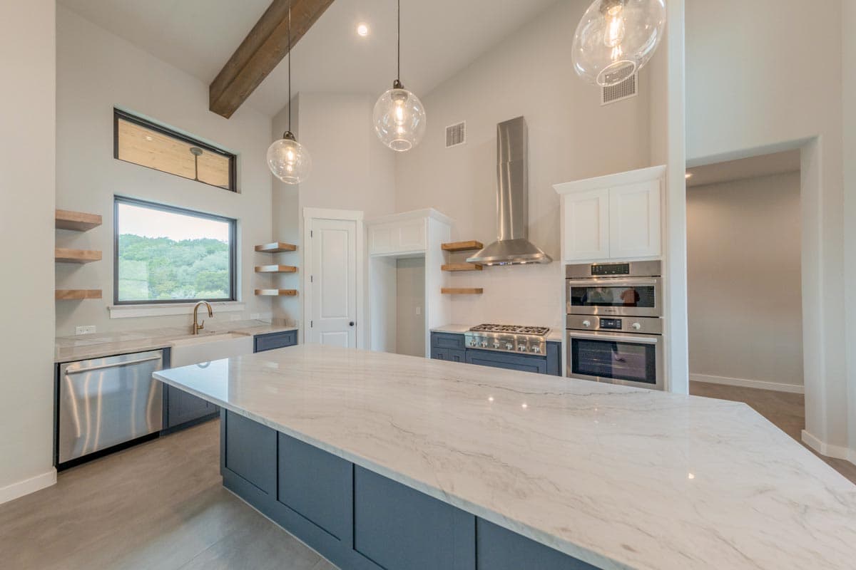 Modern kitchen with vaulted ceiling, exposed wood beam, large island, double oven, gas range, and wide windows.
