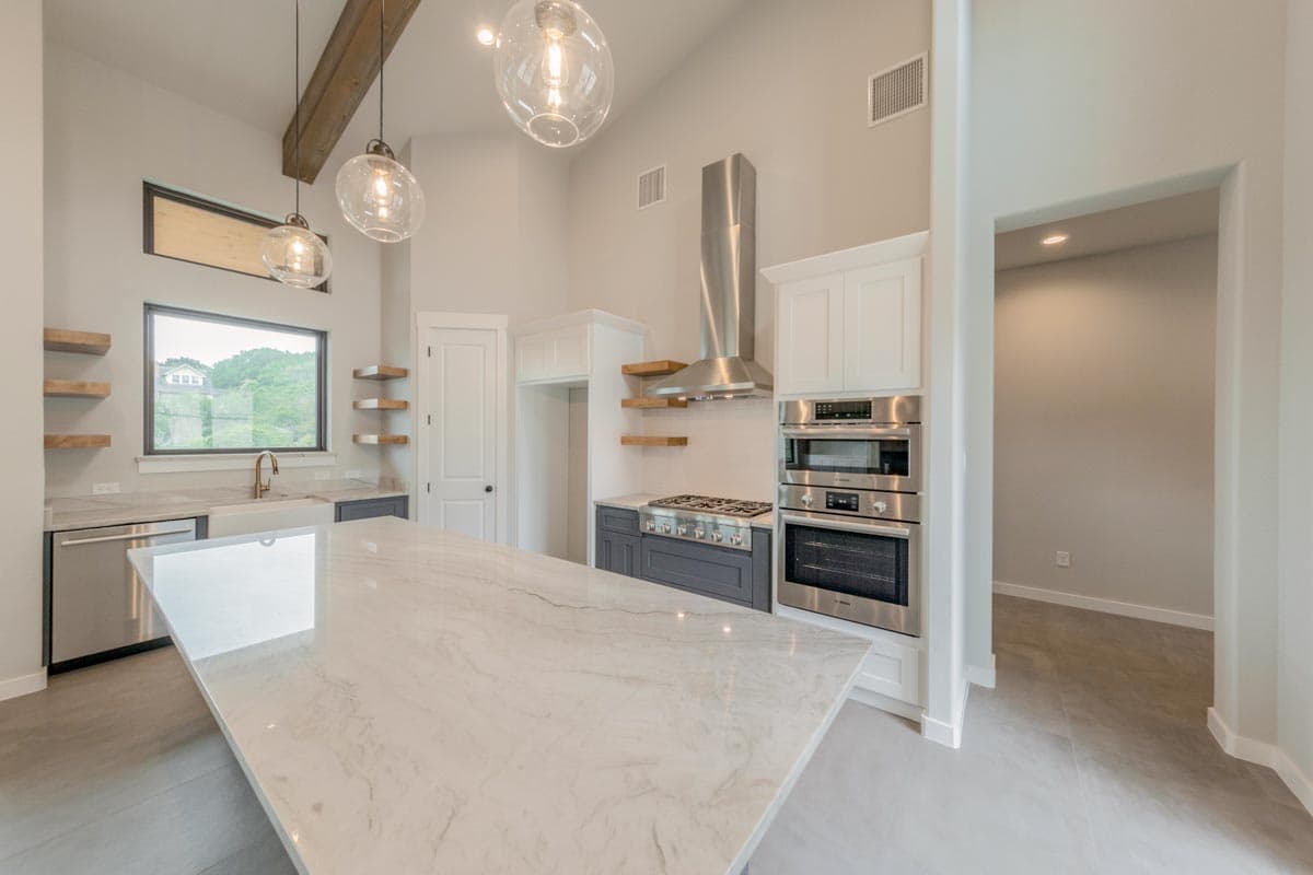 Modern kitchen with vaulted ceiling, wood beams, large island, stainless steel appliances, and range.