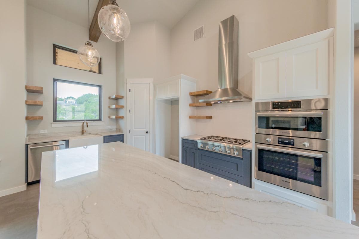 Kitchen with marble island, gas range, double ovens, stainless steel hood, and open shelving.
