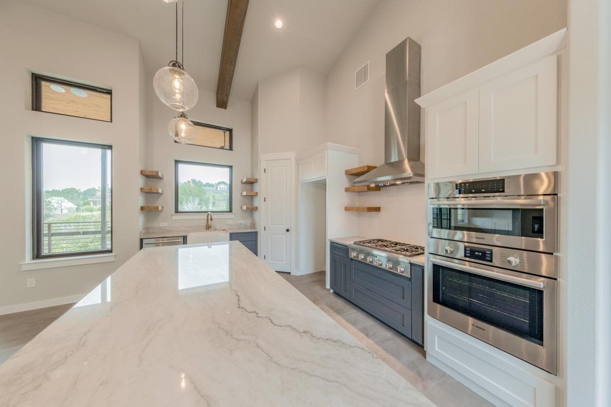 Modern kitchen with a large marble island, stainless steel appliances, gas range, and vaulted ceiling with exposed beams.