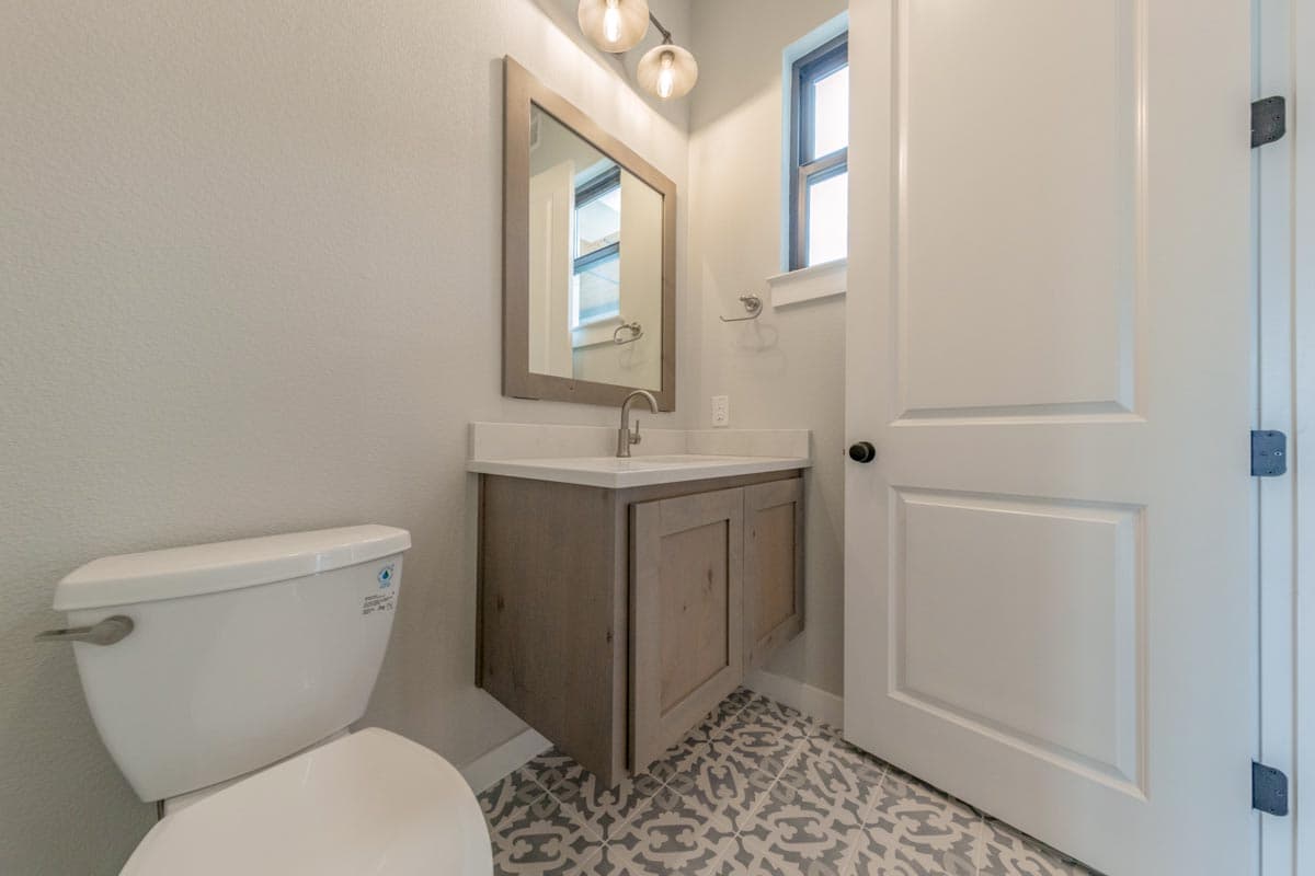 Bathroom interior with floating vanity, patterned floor tiles, toilet, and interior door.