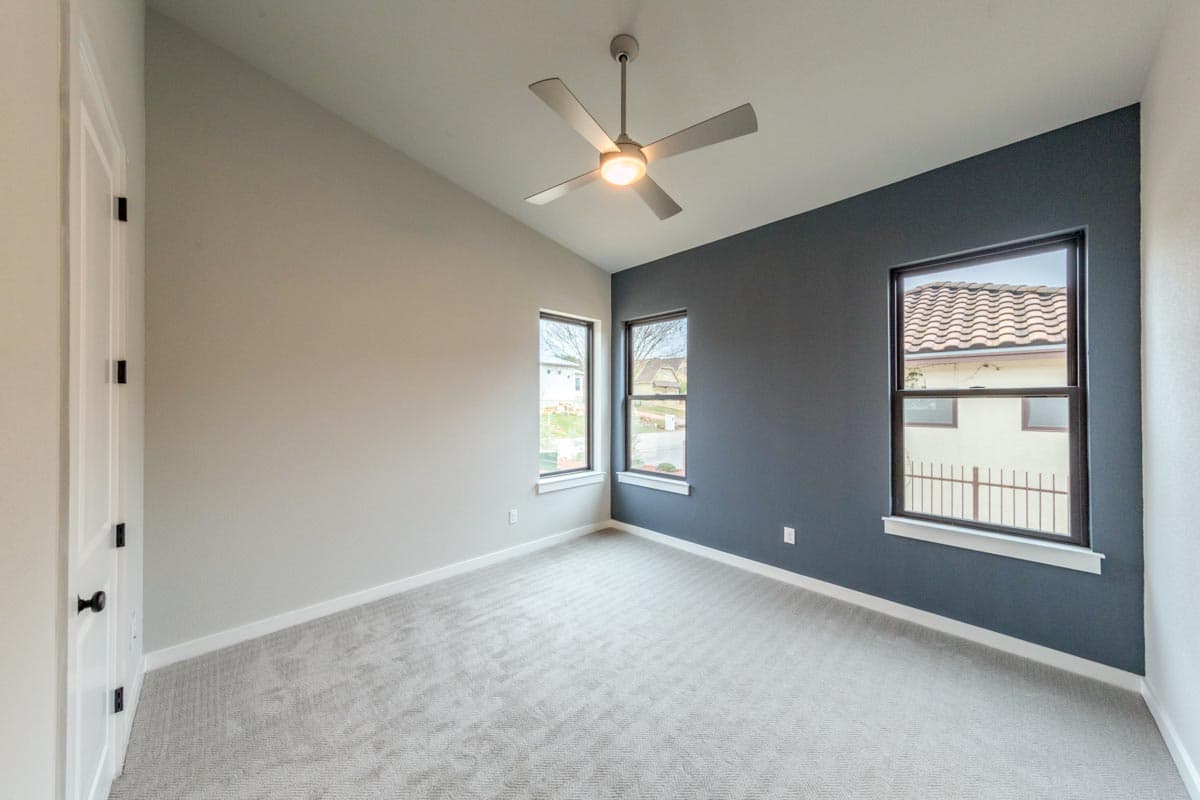 Interior view of empty bedroom with vaulted ceiling, modern ceiling fan, and three windows.