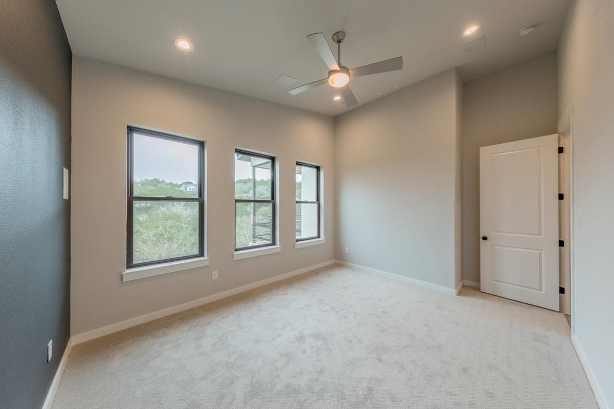 Interior view of a room with three large windows, ceiling fan, and a white paneled door.