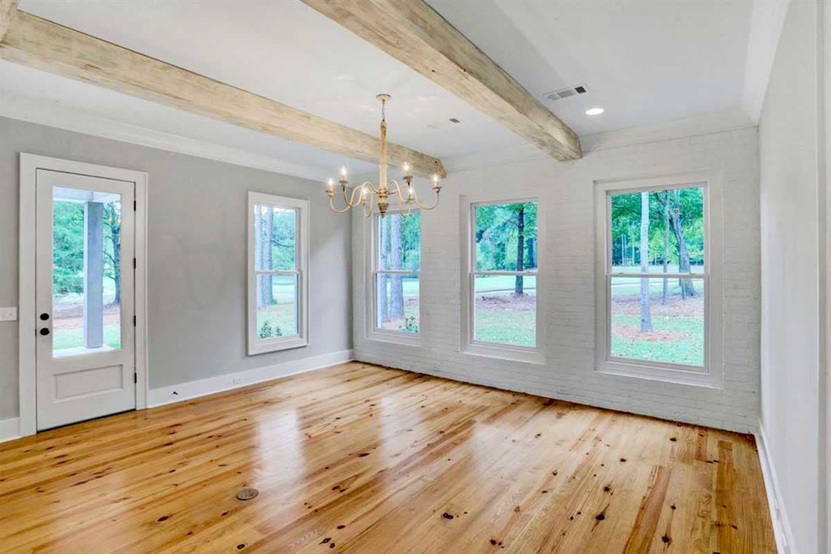 Interior view of a room with exposed wooden beams, a chandelier, pine flooring, and large windows.