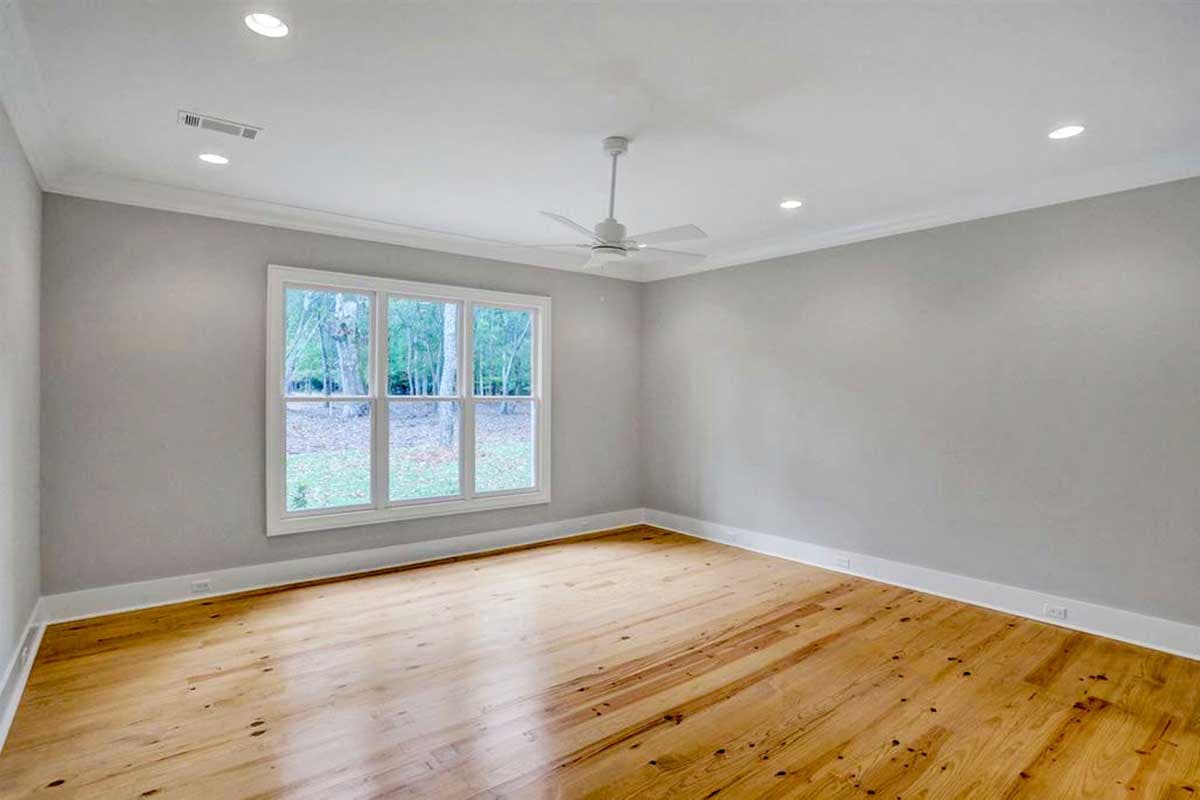 Interior view of an empty room with hardwood floors, a large multi-pane window, ceiling fan, and recessed lighting.