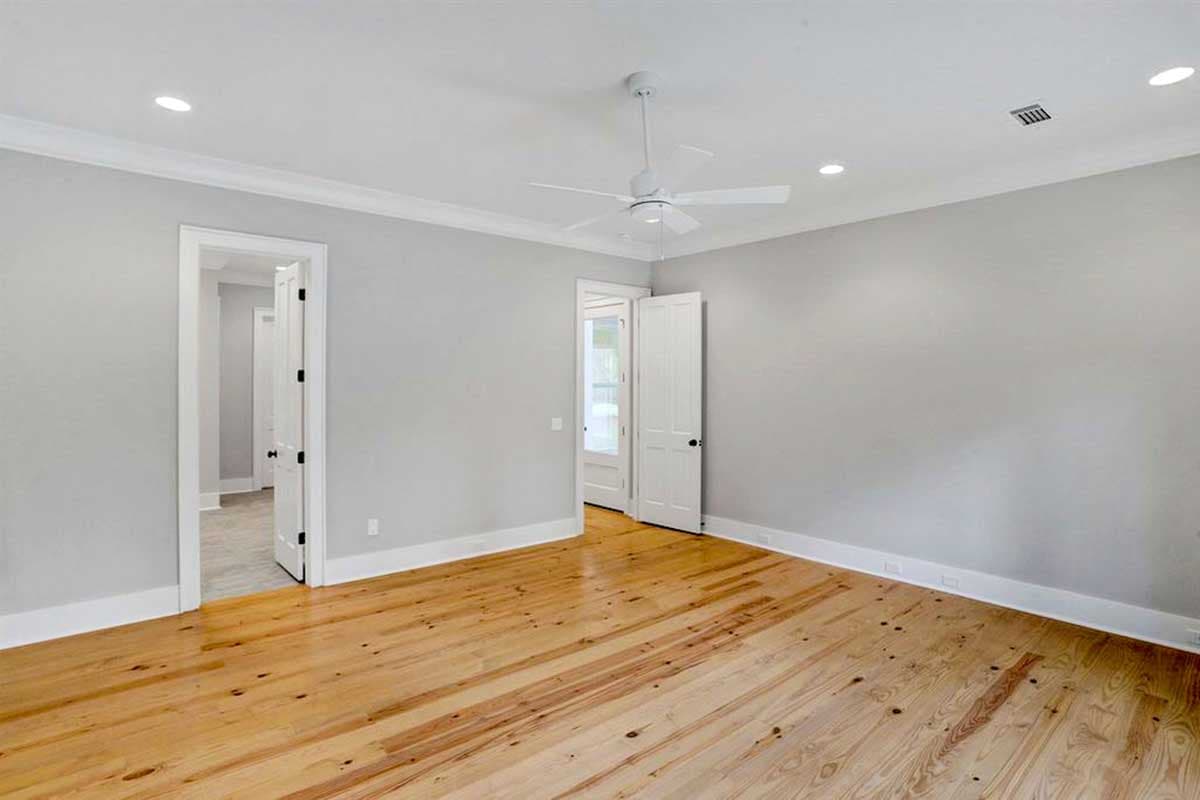 Interior view of a bedroom with light gray walls, wood floors, ceiling fan, recessed lighting, and two interior doors.