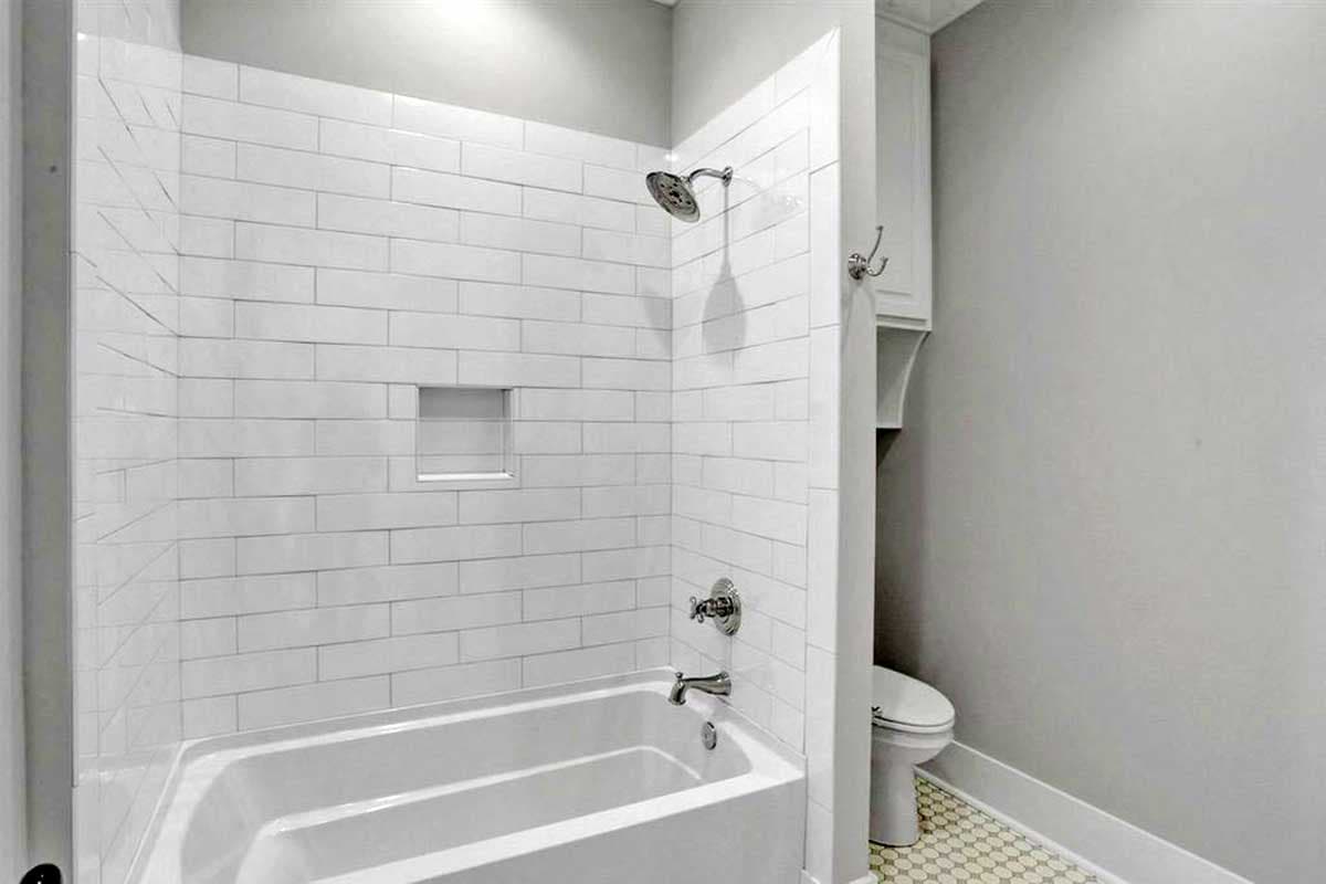 Bathroom with white subway tile shower enclosure, alcove, tub, chrome fixtures, and toilet with hexagonal floor tiles.