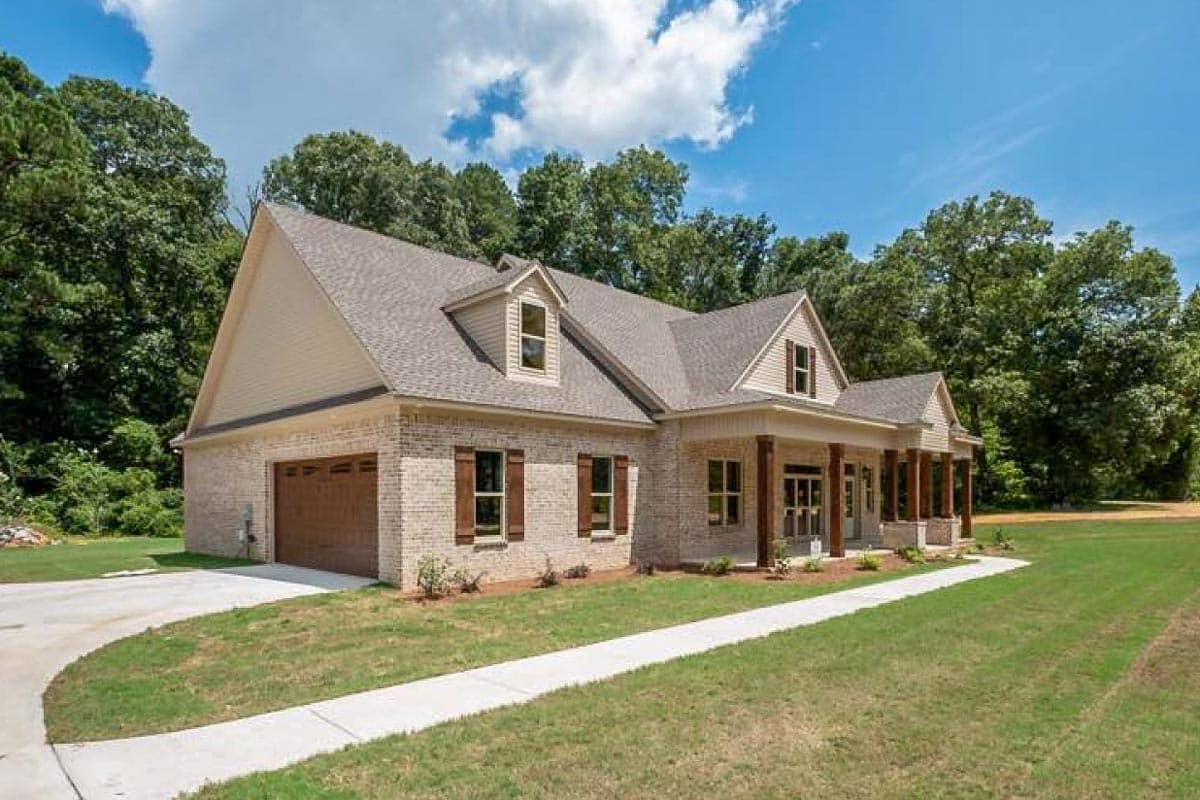 House plan exterior with light brick, gabled dormers, covered porch with columns, and attached side-entry garage.