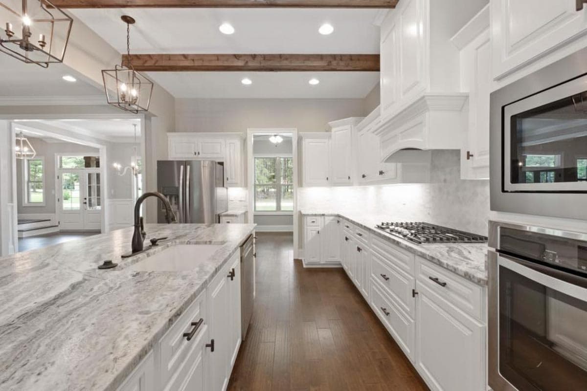 Kitchen with white cabinets, island sink, gas range, and exposed wood beams in ceiling.